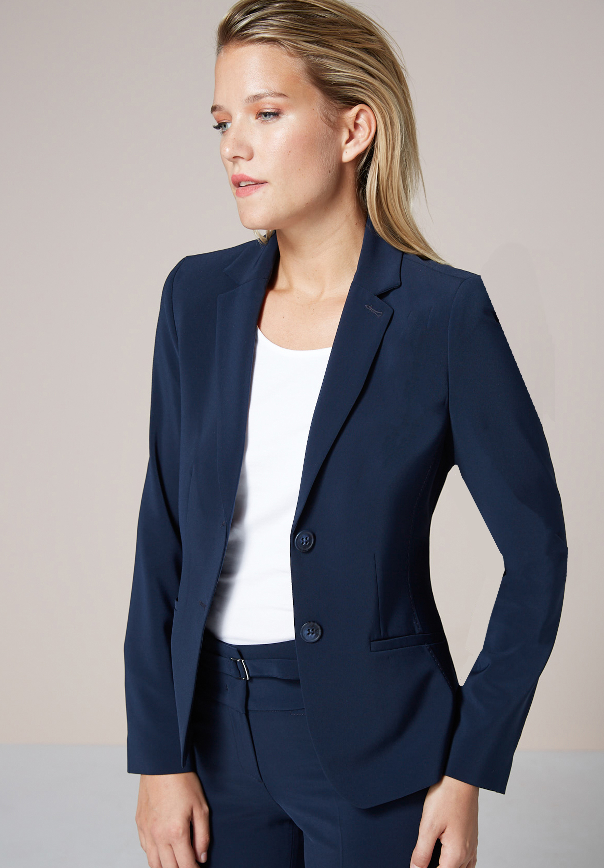 Kurzblazer EDITH Eine Person mit langen blonden Haaren trägt eine marineblaue Anzugsjacke über einem weißen Oberteil, steht mit einer Hand in der Hüfte und blickt leicht zur Seite vor einem neutralen Hintergrund.