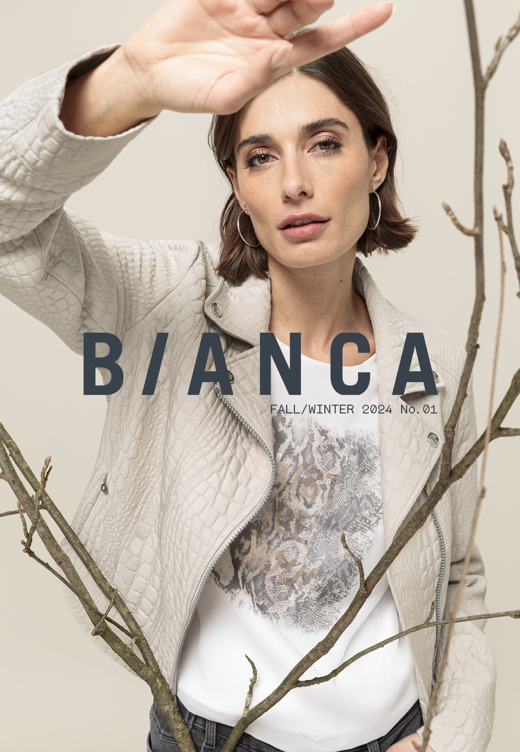 Eine Frau in einer strukturierten hellgrauen Jacke steht hinter blattlosen Zweigen und hebt einen Arm. Die Worte BIANCA und HERBST/WINTER 2024 Nr. 01 sind in großen Buchstaben über das Bild gelegt.