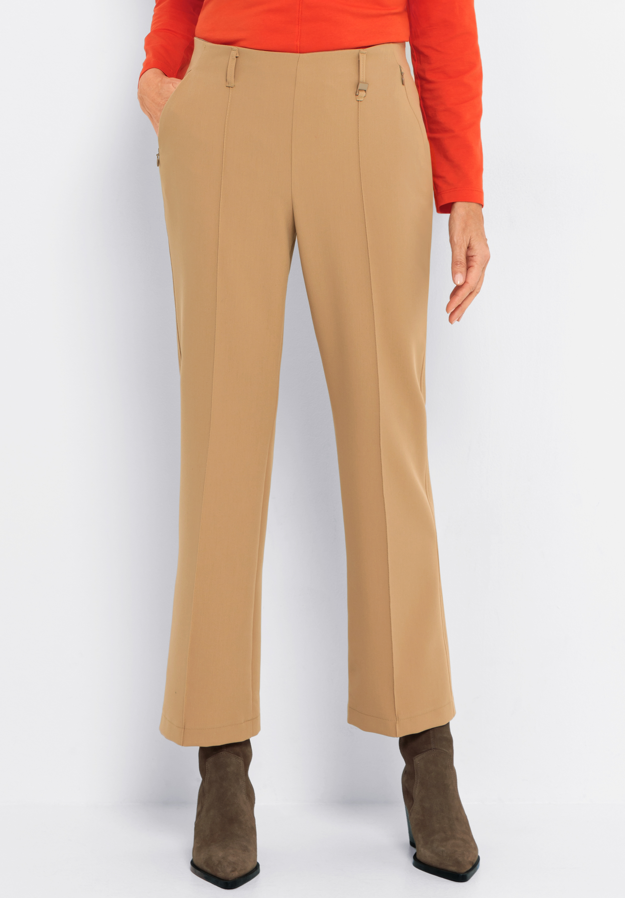 Stretch-Hose SIENA Eine Person, die eine hellbraune Anzughose, ein rotes langärmeliges Oberteil und braune Wildlederstiefel trägt, steht vor einem schlichten weißen Hintergrund. Nur die untere Hälfte des Körpers ist sichtbar.