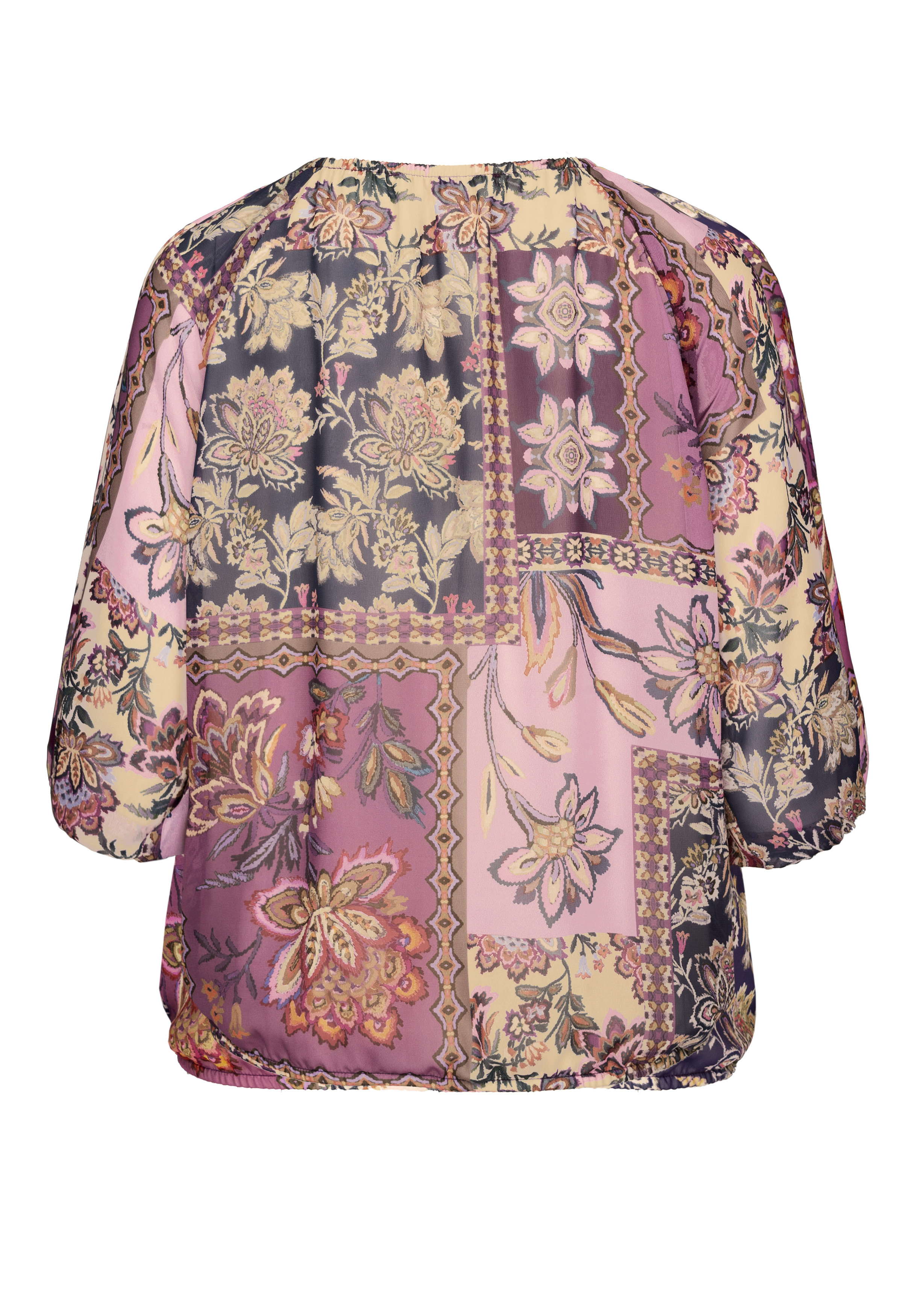 Eine locker sitzende, langärmelige Bluse mit einem Patchwork-Blumenmuster in Lila-, Rosa- und Beigetönen, von hinten gesehen. Die Bluse hat einen runden Halsausschnitt und einen leicht gerafften Saum.
