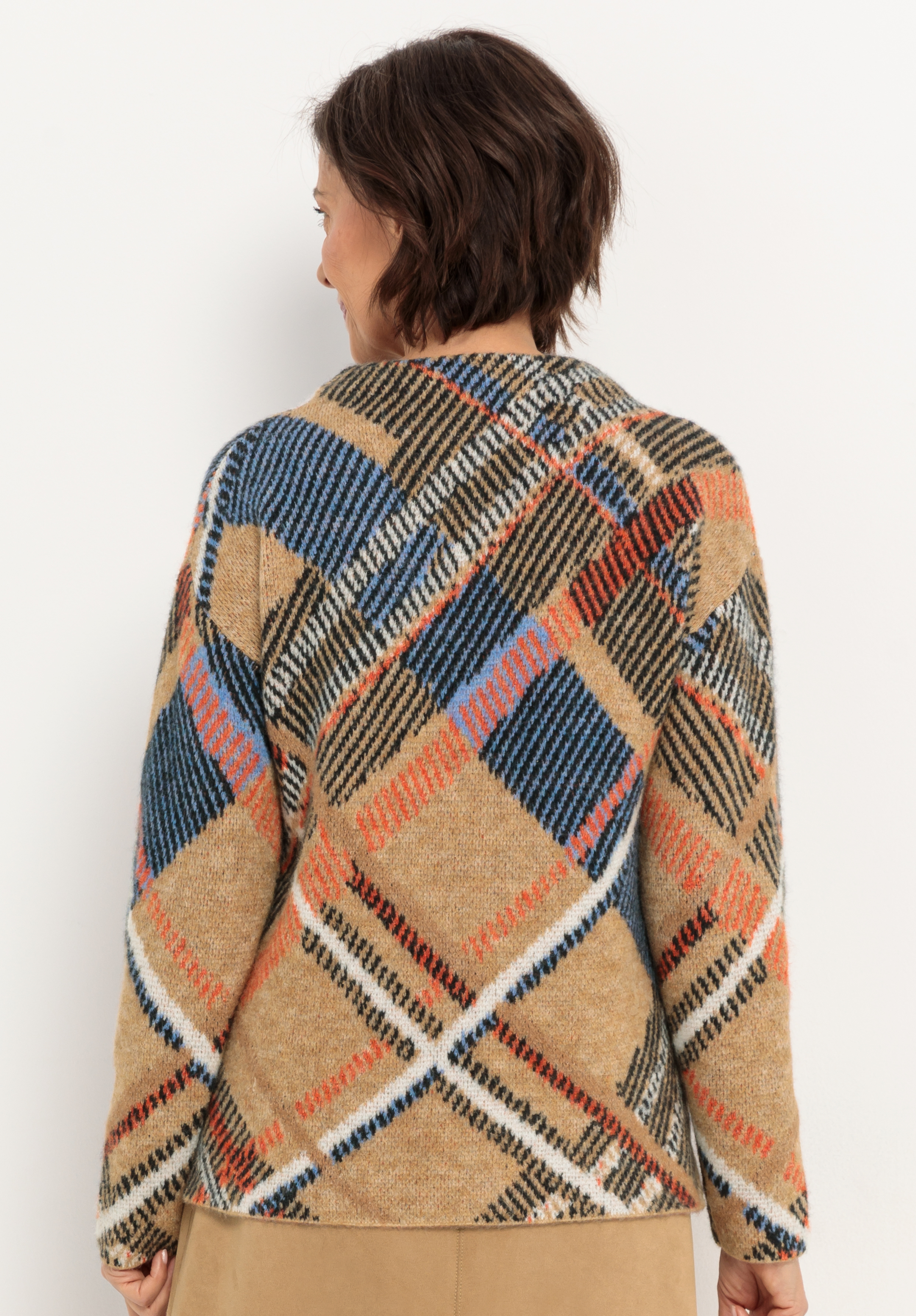 Eine Person mit kurzen braunen Haaren, von hinten gesehen, trägt einen hellbraunen Pullover mit einem auffälligen Karomuster in Blau-, Schwarz-, Orange- und Cremetönen. Der Pullover wirkt weich und gemütlich. Der Hintergrund ist einfarbig weiß.