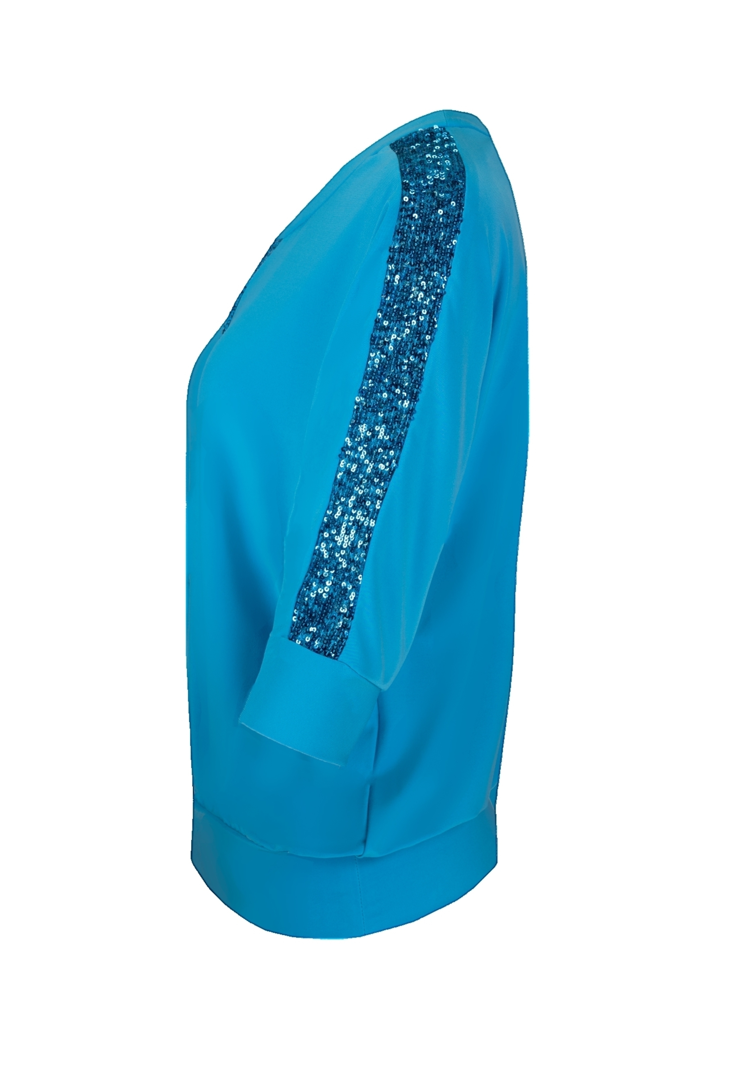 Eine leuchtend blaue Langarmbluse von der Seite mit einem breiten Streifen blauer Pailletten, der von der Schulter den Arm hinunter verläuft.