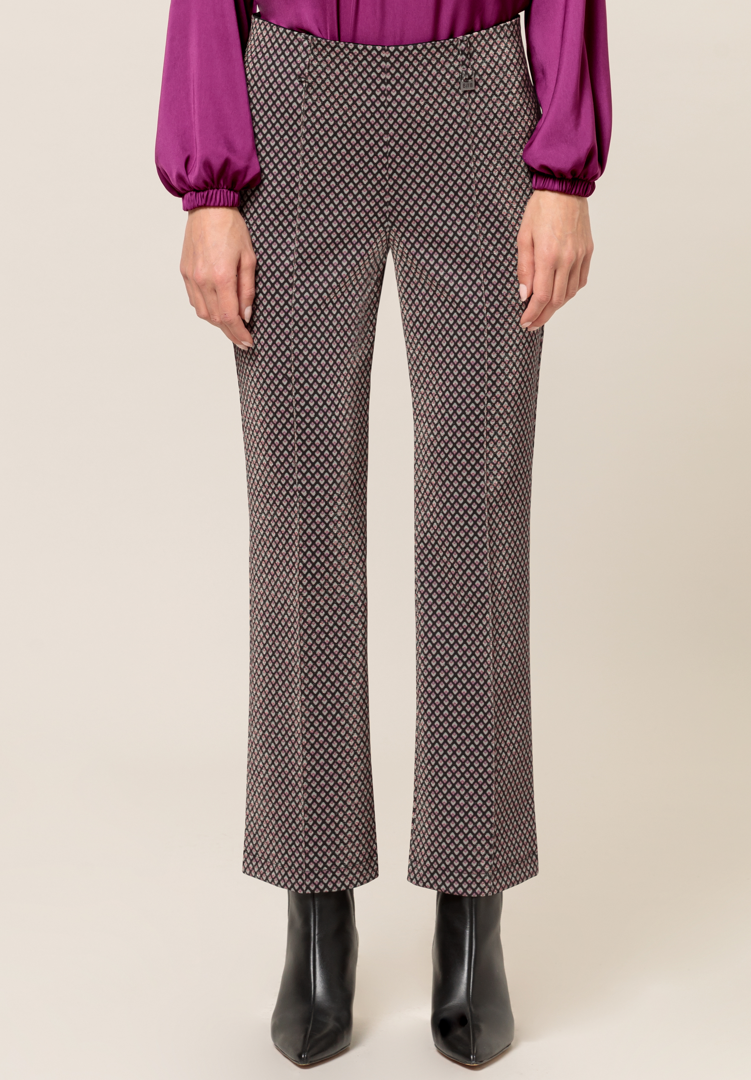 Stretch-Hose DENVER Eine Person in gemusterten, gerade geschnittenen Hosen, einer langärmeligen lila Bluse und schwarzen spitzen Stiefeletten steht vor einem schlichten Hintergrund. Das Bild ist am Oberkörper abgeschnitten.