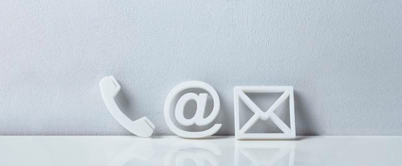 Drei weiße Symbole – ein Telefonhörer, ein At-Zeichen (@) und ein Umschlag – sind in einer Reihe vor einem hellgrauen Hintergrund angeordnet und stellen die Kommunikationsmethoden dar: Telefon, E-Mail und Post.