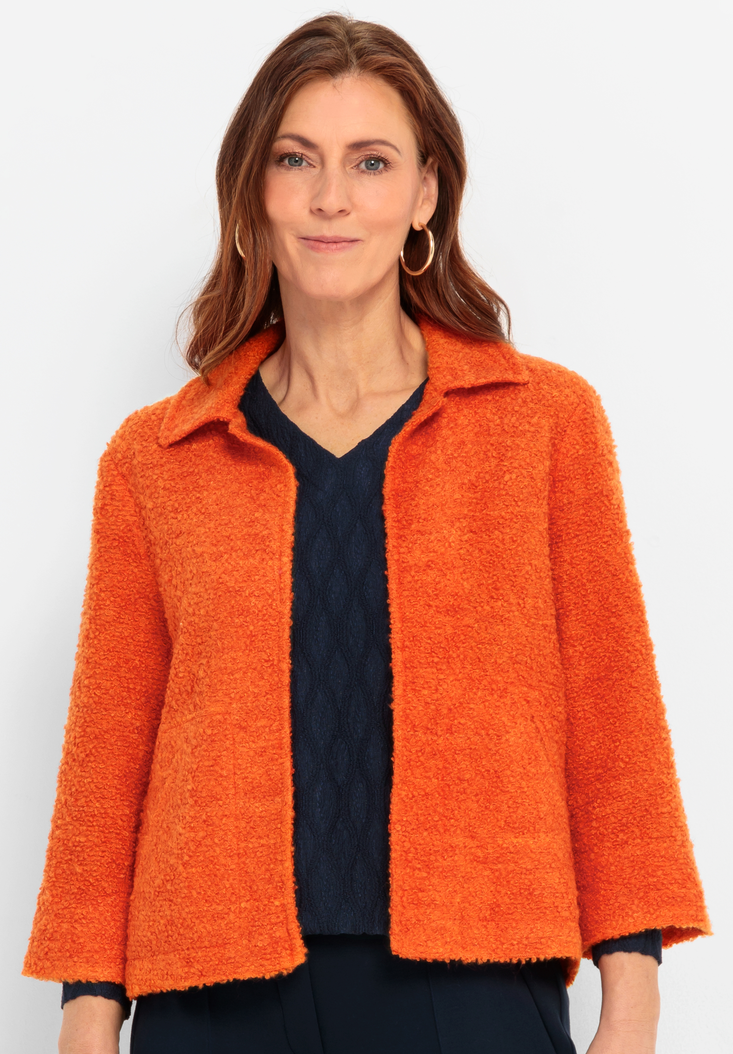 Kurzblazer KATE Eine Frau mit langen braunen Haaren, die eine strukturierte orangefarbene Jacke über einem marineblauen Oberteil trägt, steht vor einem schlichten weißen Hintergrund und lächelt sanft in die Kamera.
