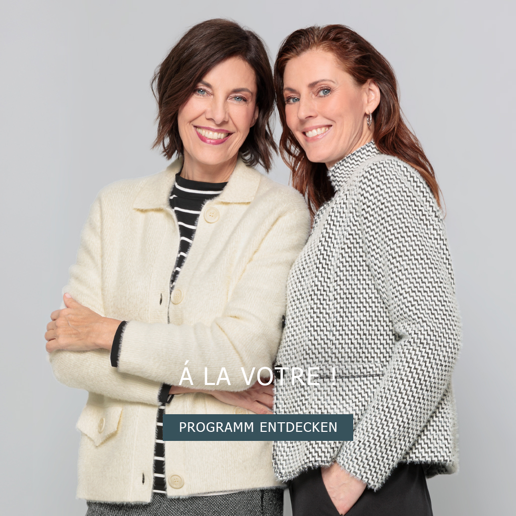Zwei Frauen lächeln. Beide mit gemusterte Jacken; linke Frau hat eine cremefarbene Jacke über einem gestreiften Oberteil, rechte Frau trägt strukturierte helle Jacke. Á LA VOTRE! PROGRAMM ENTDECKEN.