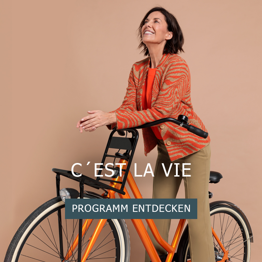 Eine lächelnde Frau in einer orange gemusterten Jacke und einer beigen Hose steht neben einem orangefarbenen Fahrrad vor einem beigen Hintergrund. Der Text lautet CEST LA VIE und PROGRAMM ENTDECKEN.