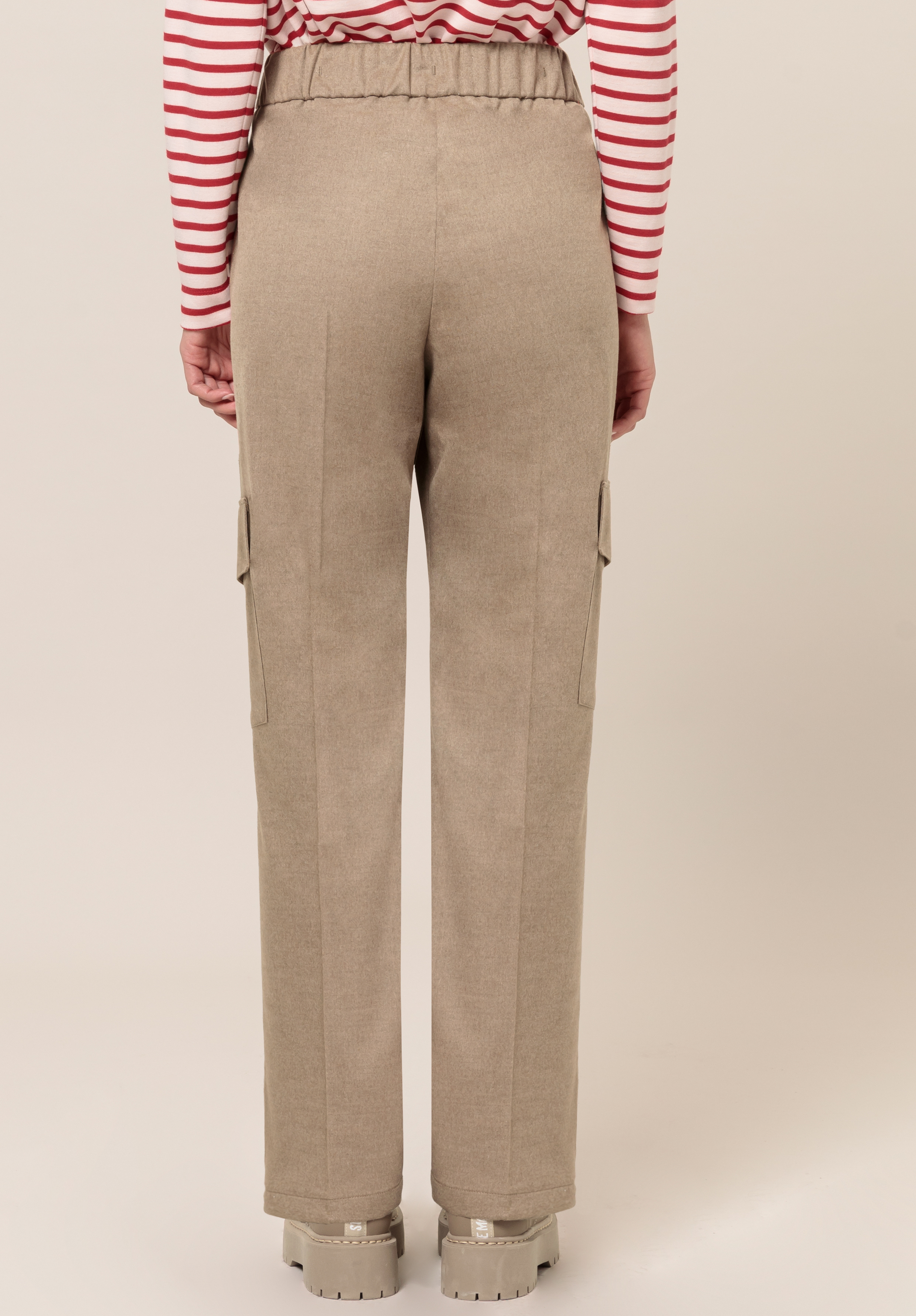 Eine Person trägt eine beige Hose mit geradem Bein und Seitentaschen sowie ein rot-weiß gestreiftes Langarmhemd. Die Hose hat einen elastischen Bund und die Person trägt klobige beige Schuhe.