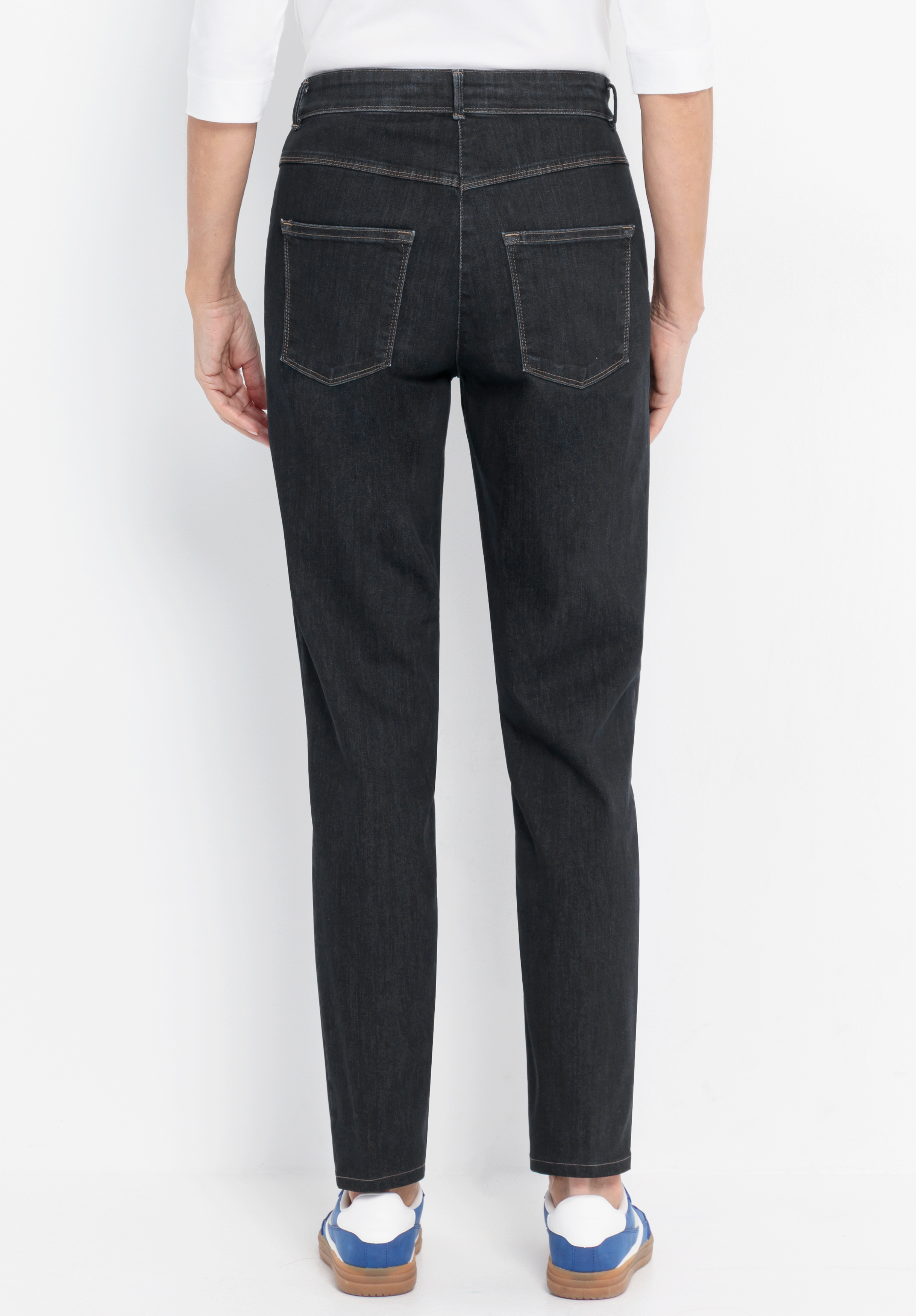 Eine Person, die eine dunkelblaue Jeans mit geradem Bein und blau-weiße Sneaker trägt, ist von hinten vor einem schlichten weißen Hintergrund zu sehen.