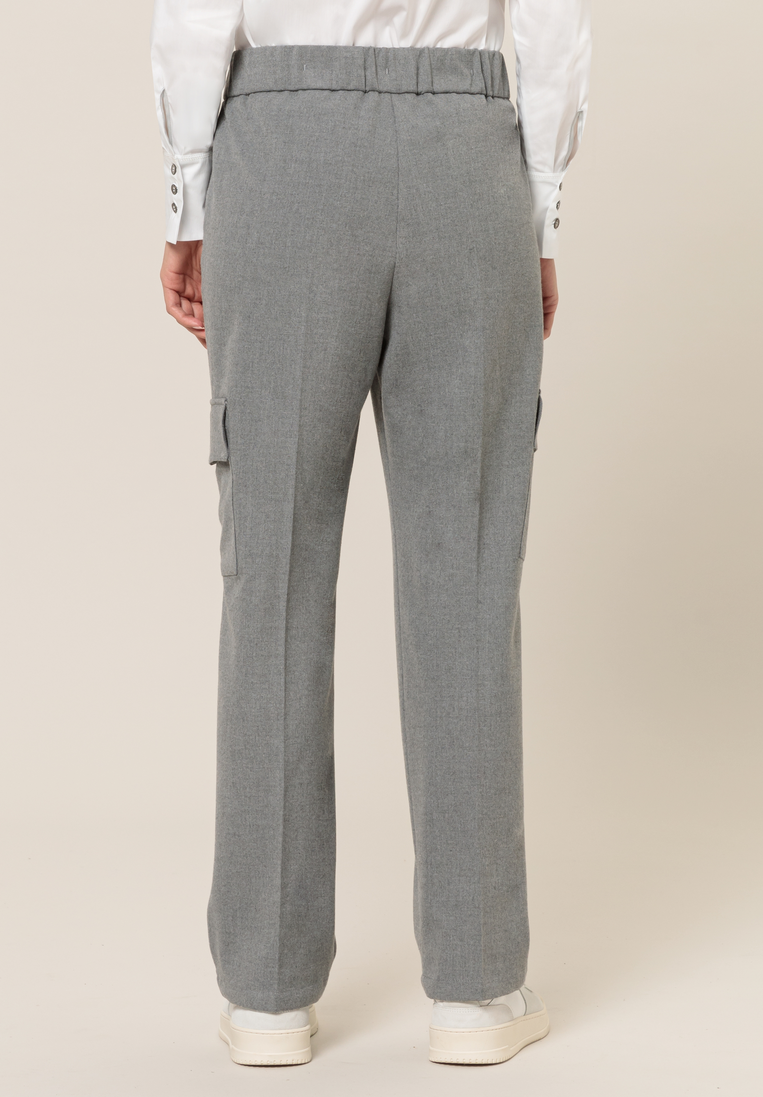 Eine Person, die eine graue Hose mit geradem Bein und Seitentaschen, weiße Turnschuhe und ein weißes Button-Down-Hemd trägt, ist von hinten vor einem einfarbigen Hintergrund zu sehen.