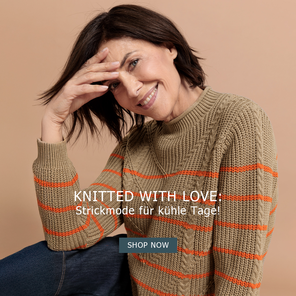 Eine lächelnde Frau mit braunen Haaren trägt einen beigefarbenen Strickpullover mit orangenen Streifen. Sie sitzt lässig da und stützt ihre Hand auf die Stirn. Text: Mit Liebe gestrickt: Strickmode für kühle Tage! Jetzt einkaufen.